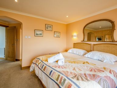 A bedroom with a double bed a quilt a wooden framed mirror and three pictures on the wall at Trevan House Lundy in Polzeath