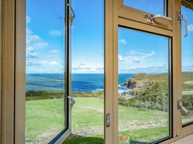 A view of the ocean and grassy hills through an open window at Trevan House (Lundy) in Polzeath