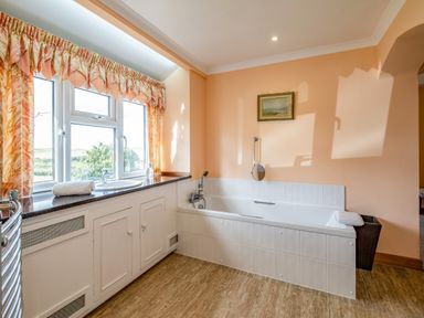 A bathroom with a bathtub a window with curtains and cabinets beneath a countertop at Trevan House Lundy in Polzeath