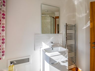 A bathroom sink with a faucet and mirror above next to a chrome towel radiator and a partially visible wooden door at Trevan House Lundy in Polzeath