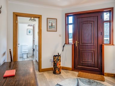 An entryway with a wooden door a rug an umbrella stand a wooden table a chair and a view into a bathroom at Trevan House Lundy in Polzeath