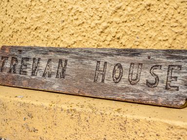 A wooden sign with the words Trevan House against a textured yellow wall at Trevan House (Lundy) in Polzeath