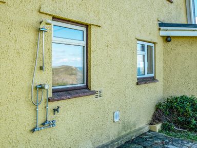 An exterior wall of a yellow building with two windows a mounted outdoor shower and a garden bush at Trevan House Lundy in Polzeath