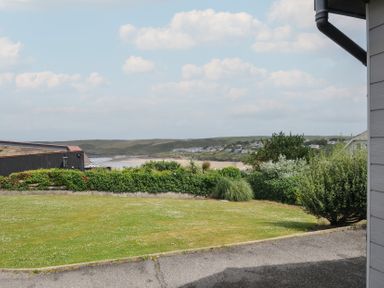 A view of a grassy area with hedges and buildings at Hillview in Polzeath