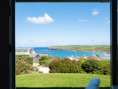 View of a coastline with houses trees and grass from inside a building at Windyhill Polzeath