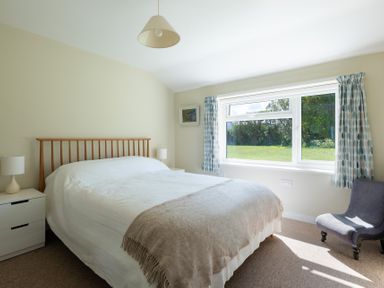 A bedroom with a bed a bedside table with lamps a chair and a window with curtains at Windyhill Polzeath