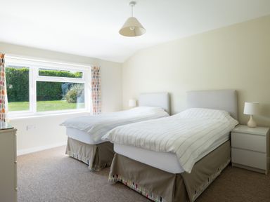 A bedroom with two single beds nightstands lamps window with curtains at Windyhill in Polzeath