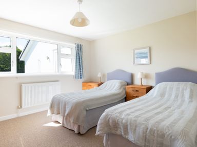 A bedroom with two single beds two wooden bedside tables with lamps a window and a framed picture at Windyhill Polzeath