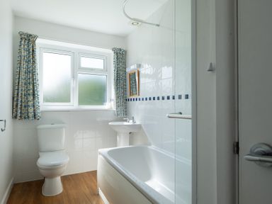 A bathroom with a toilet sink bathtub window with curtains and tiled walls at Windyhill in Polzeath