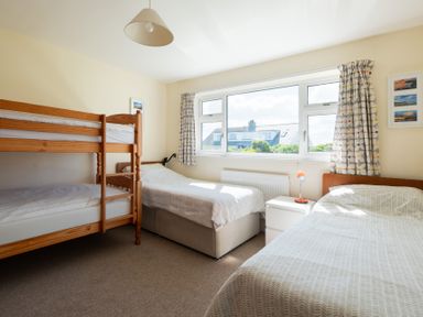 A bedroom with bunk beds two single beds a bedside table with a lamp and a window with curtains at Windyhill in Polzeath