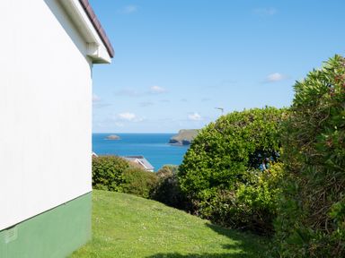 A green lawn and bushes beside a white house with the sea and islands in the background at Windyhill in Polzeath