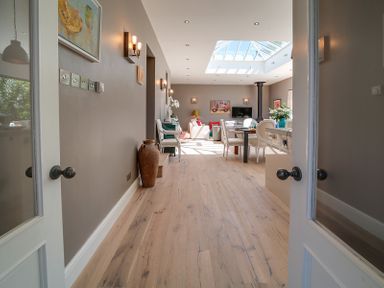 A view through open double doors into a living and dining area with wooden floors skylight and furniture at Trevanion in Rock