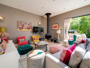 A living room with colorful chairs a round coffee table and a hanging fireplace at Trevanion in Rock