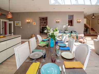 A dining room with a wooden table set with plates and colorful napkins and white chairs at Trevanion in Rock