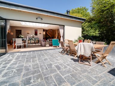 An open plan room with dining table and chairs inside and patio table with chairs outside on stone tiled floor at Trevanion Rock