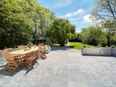 A patio with a wooden table and chairs surrounded by trees and grass at Trevanion in Rock