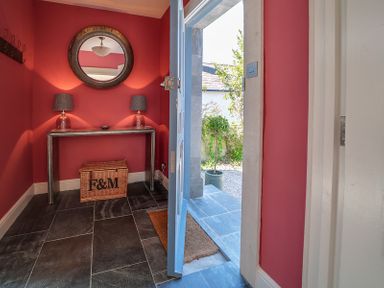 An entryway with red walls a console table two lamps a round mirror and a wicker basket at Trevanion in Rock