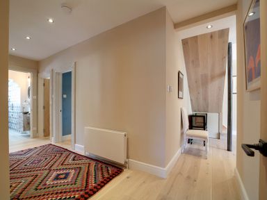A hallway with a patterned rug a radiator two doorways and a chair under slanted wooden ceiling at Trevanion in Rock