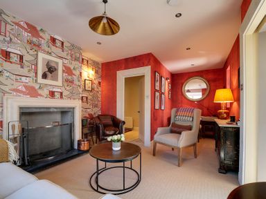 A living room with patterned wallpaper a fireplace a round coffee table and armchairs at Trevanion in Rock