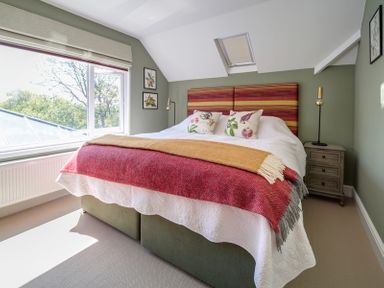A bedroom with a bed featuring patterned pillows and blankets a bedside table and framed pictures on the wall at Trevanion in Rock
