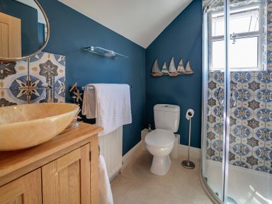 A bathroom with a wooden sink cabinet white toilet glass shower enclosure and blue walls at Trevanion in Rock