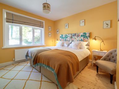 A bedroom with two single beds pushed together with patterned headboards and blankets on a rug next to a window at Trevanion in Rock