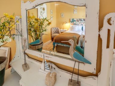A mirror on a white wooden dresser reflecting a bedroom with a bed and chair at Trevanion in Rock