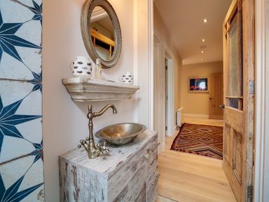 A hallway with a wooden door a patterned rug a rustic sink with a brass faucet and a round mirror at Trevanion in Rock