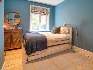 A bedroom with blue walls a white bed with pillows a wooden cabinet with a round mirror and a floor lamp at Trevanion in Rock