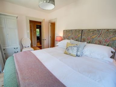 A bedroom with a bed with patterned headboard and decorative pillows a white wardrobe and a white chair at Trevanion in Rock
