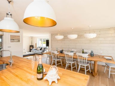 A kitchen island with a bottle of champagne and glasses overlooking a dining table with chairs and pendant lights at Seastar in Rock
