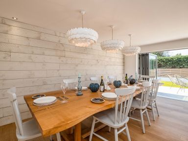 A dining room with a long wooden table set with plates and glasses and white chairs at Seastar Rock