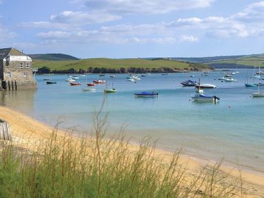 A sandy beach with vegetation in the foreground boats anchored in a bay and a stone building on the left at Seastar in Rock