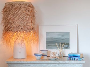 A dresser with a lamp with a fringed shade bowls coral decoration reed diffuser books and a painting at Seastar in Rock