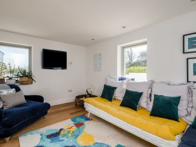 A living room with a blue armchair, a white sofa with yellow and green cushions, a colorful rug, and a wall-mounted TV at Seastar in Rock