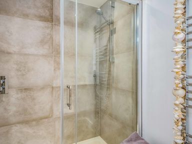 A shower with glass door and tiled walls next to a towel rack with shells at Seastar in Rock