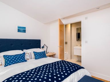 A bedroom with a bed featuring a blue headboard and blue patterned pillows and throw with an open door leading to a bathroom at Seastar in Rock
