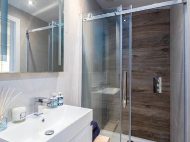 A bathroom with a sink and soap dispensers and a glass door shower with wood paneling at Seastar in Rock