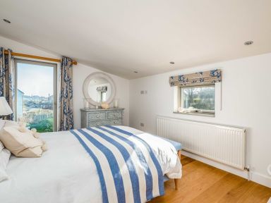 A bedroom with a bed covered by a white and blue striped blanket beside a window and a chest of drawers with a round mirror at Seastar Rock