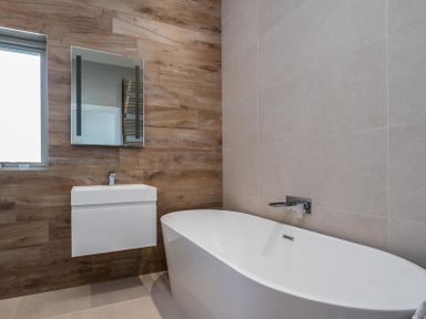 A bathroom with a white bathtub a wall-mounted sink a rectangular mirror and wood and tile walls at Seastar in Rock