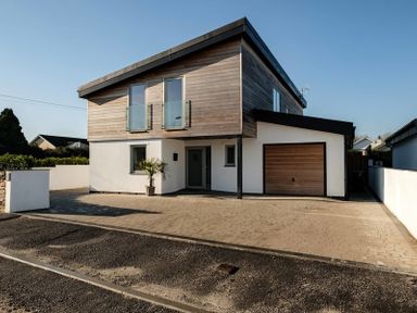 A modern two-story house with wooden cladding and white walls with a driveway and garage at Seastar in Rock