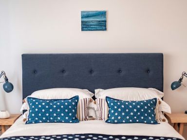 A bedroom with a blue upholstered headboard blue patterned pillows and lamps on wooden bedside tables at Seastar in Rock