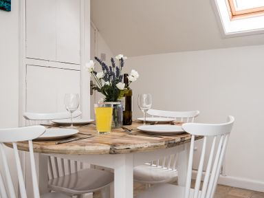 A dining table with white chairs plates glasses a glass of orange juice a bottle and a vase with flowers at Pinewood 14 in Polzeath