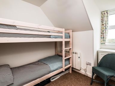 A bedroom with a wooden bunk bed a green chair and a window with floral curtains at Pinewood 14 in Polzeath
