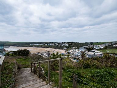 A view of a beach town with a sandy beach and houses seen from a wooden staircase on a grassy hill at Pinewood 14 Polzeath