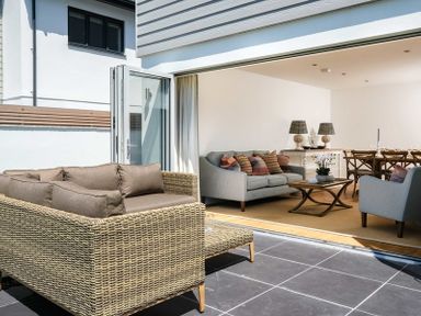 An outdoor patio with wicker sofa and an indoor living room with sofas and a wooden dining table at Artemis in Rock