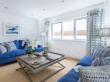 A living room with blue sofas and patterned cushions with a wooden coffee table and floral curtains at Artemis in Rock