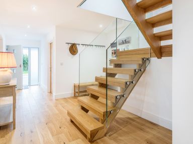 An entryway with wooden stairs and glass railing a small bench a wooden floor and a lamp on a table at Artemis in Rock
