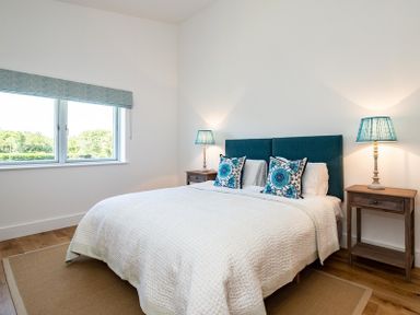 A bedroom with a double bed with blue headboard and decorative pillows between two wooden bedside tables with blue lamps at Artemis in Rock