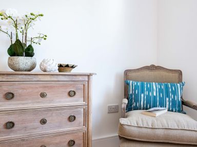 A wooden dresser with decorative items next to an armchair with a blue patterned cushion and a book at Artemis in Rock